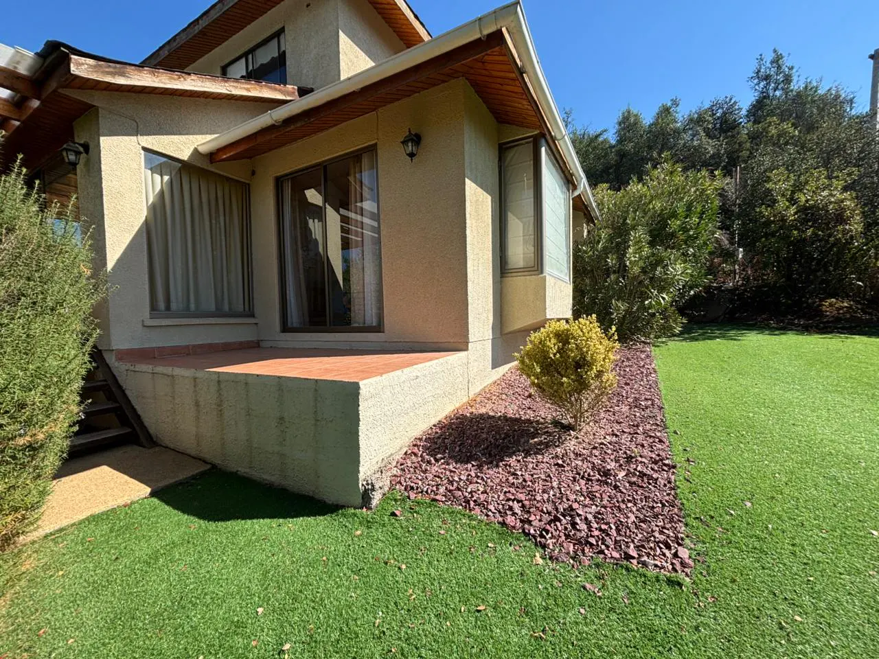 Tan two-story house with a brown roof, a red-tiled patio, and green grass.