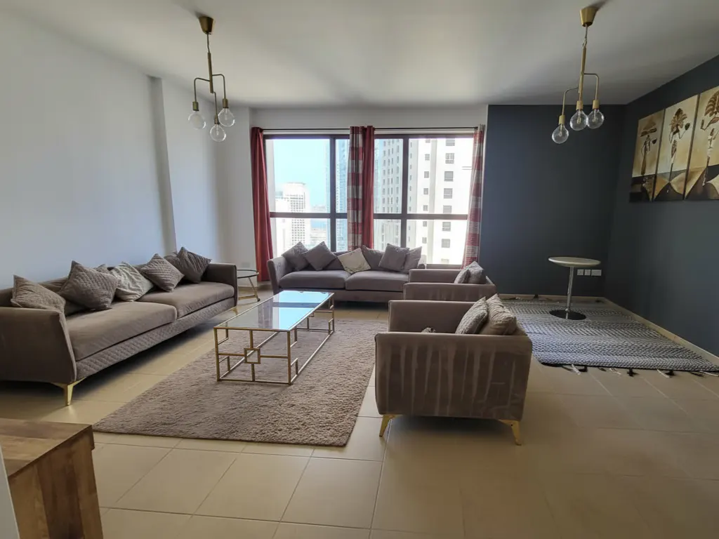 Living room with brown sofas, glass coffee table, and city view through windows with red curtains. Modern light fixtures hang from the ceiling.