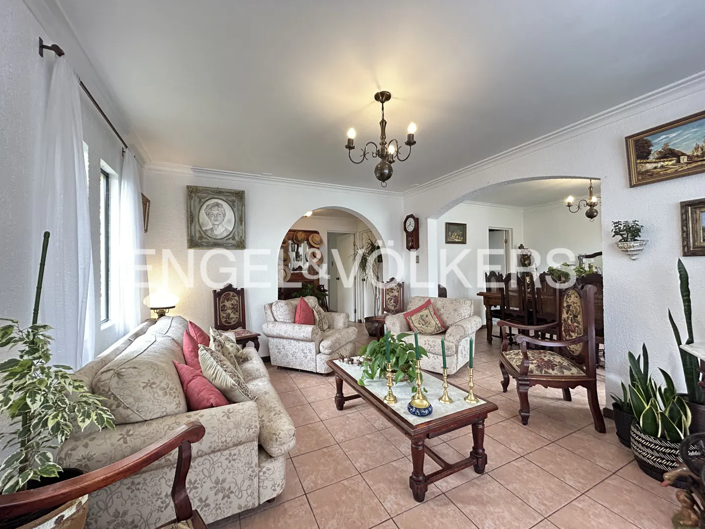 Traditional living room with beige patterned sofas, a wooden coffee table, arched doorways, and tiled floors.