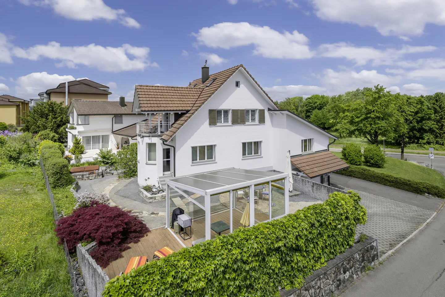 Aerial view of a white two-story house with a brown tile roof, a sunroom, and a landscaped yard on a sunny day.