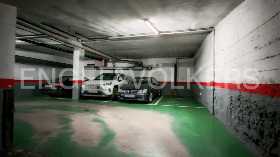 Indoor parking garage with three cars parked in designated spots. The floor is green and the walls are white with a red stripe.