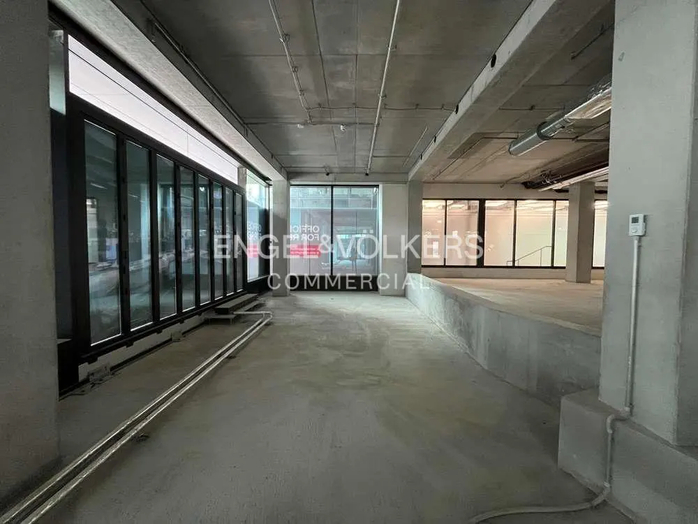 Unfinished commercial space with concrete floors, walls, and ceiling. Large windows with black frames and an Engel & Volkers sign.