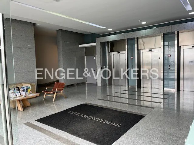 Lobby of VISTAMONTEMAR building with elevators, a wooden bench with brochures, and a brown leather chair.