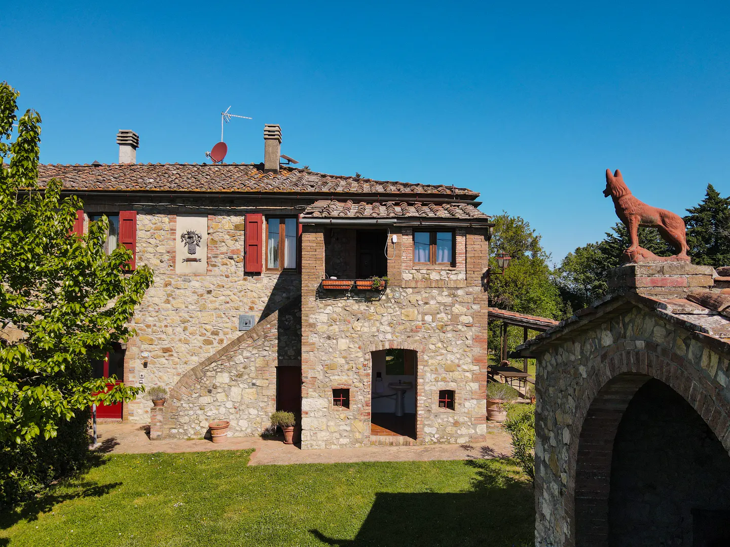 Exterior of a stone farmhouse with red shutters and a terracotta wolf statue on the roof.