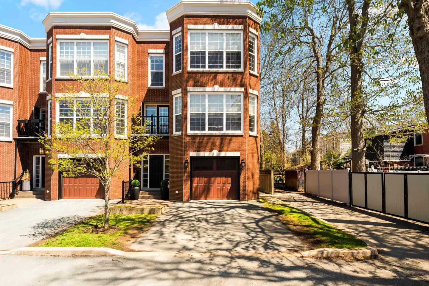Exterior of a multi-story red brick townhouse with a driveway, garage, and a small tree in the front yard.