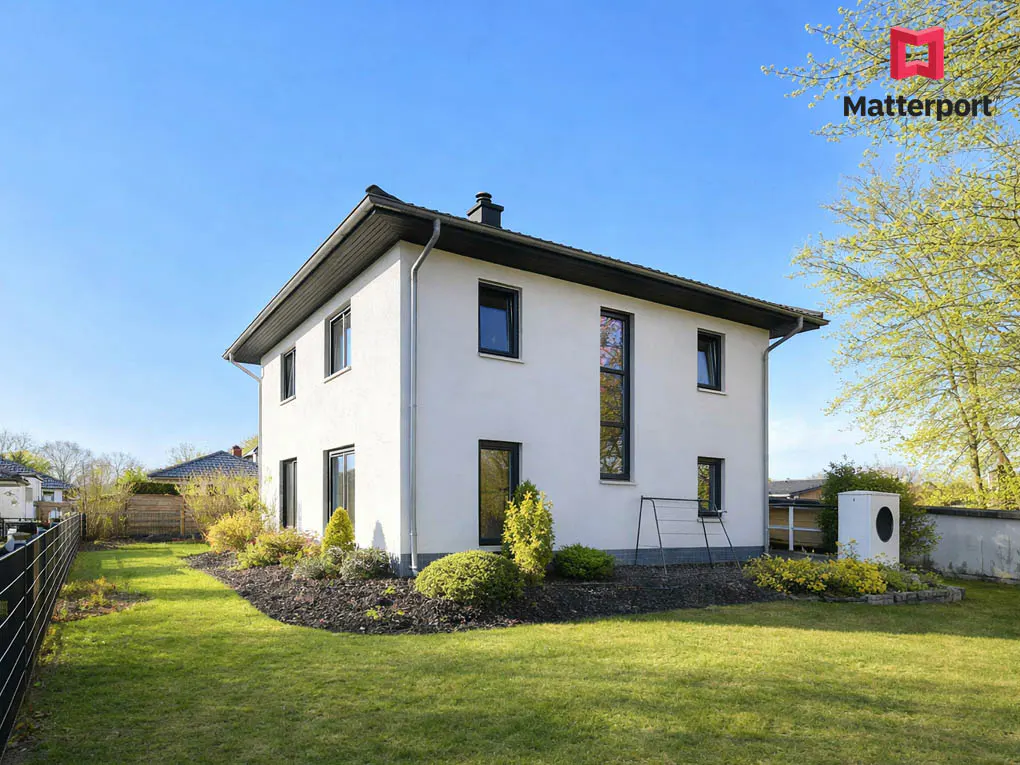 Two-story white house with black trim, surrounded by a green lawn and landscaping under a clear blue sky.