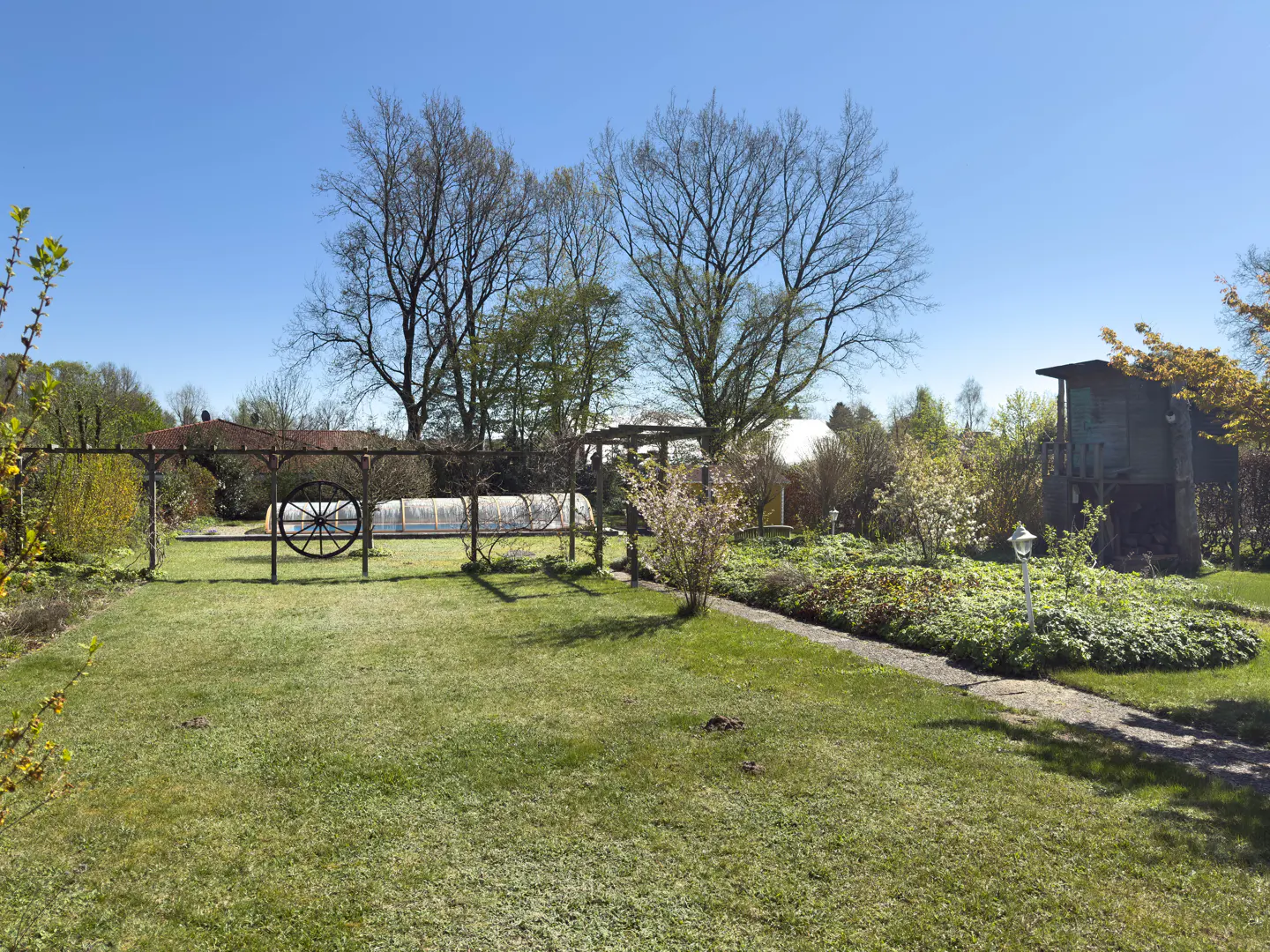 A lush green lawn with a decorative wagon wheel and a small garden shed under a clear blue sky.