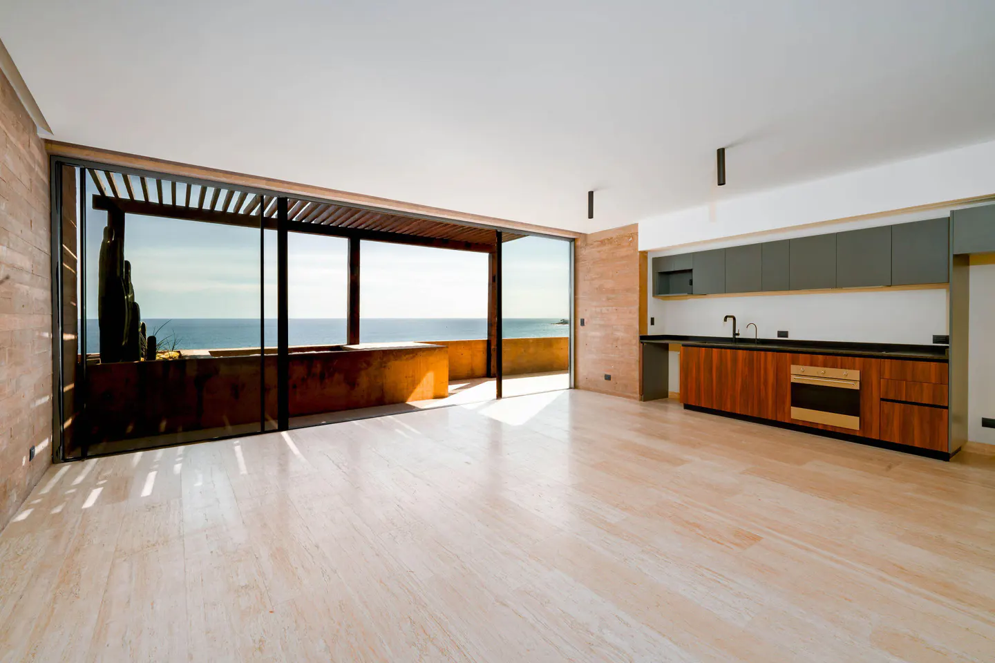 Bright, modern apartment interior with a kitchen and ocean view. Large sliding glass doors open to a balcony overlooking the sea.