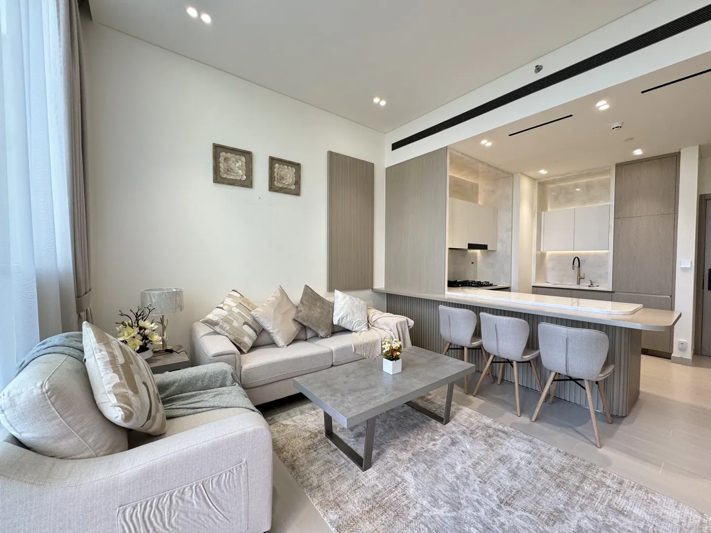 Living room with a beige sofa, gray coffee table, and open kitchen with bar stools.