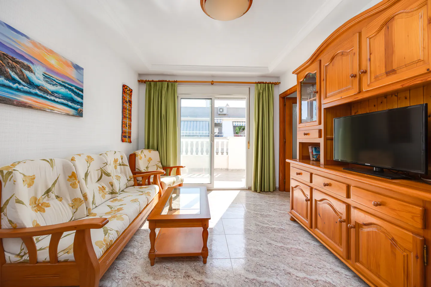 Living room with floral sofa, wooden coffee table, large entertainment unit, and sliding glass doors to a balcony.