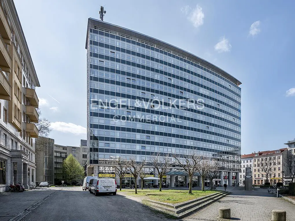 Exterior view of a tall, modern office building with many windows, Engel & Völkers logo, and street view.