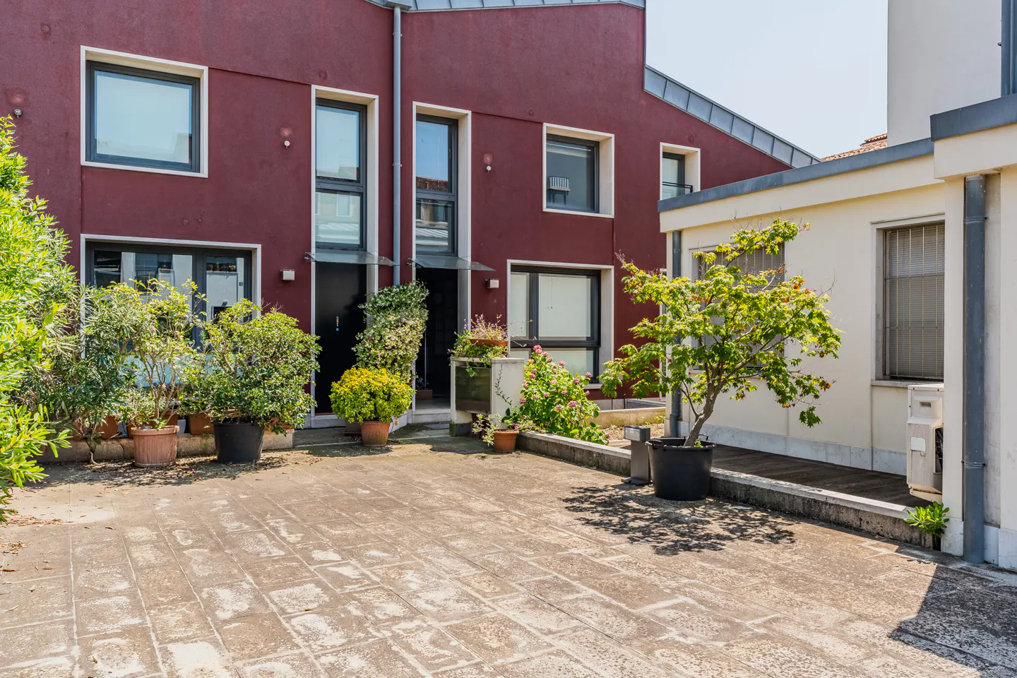 Exterior view of a red building with black windows and doors, a stone patio, and potted plants.