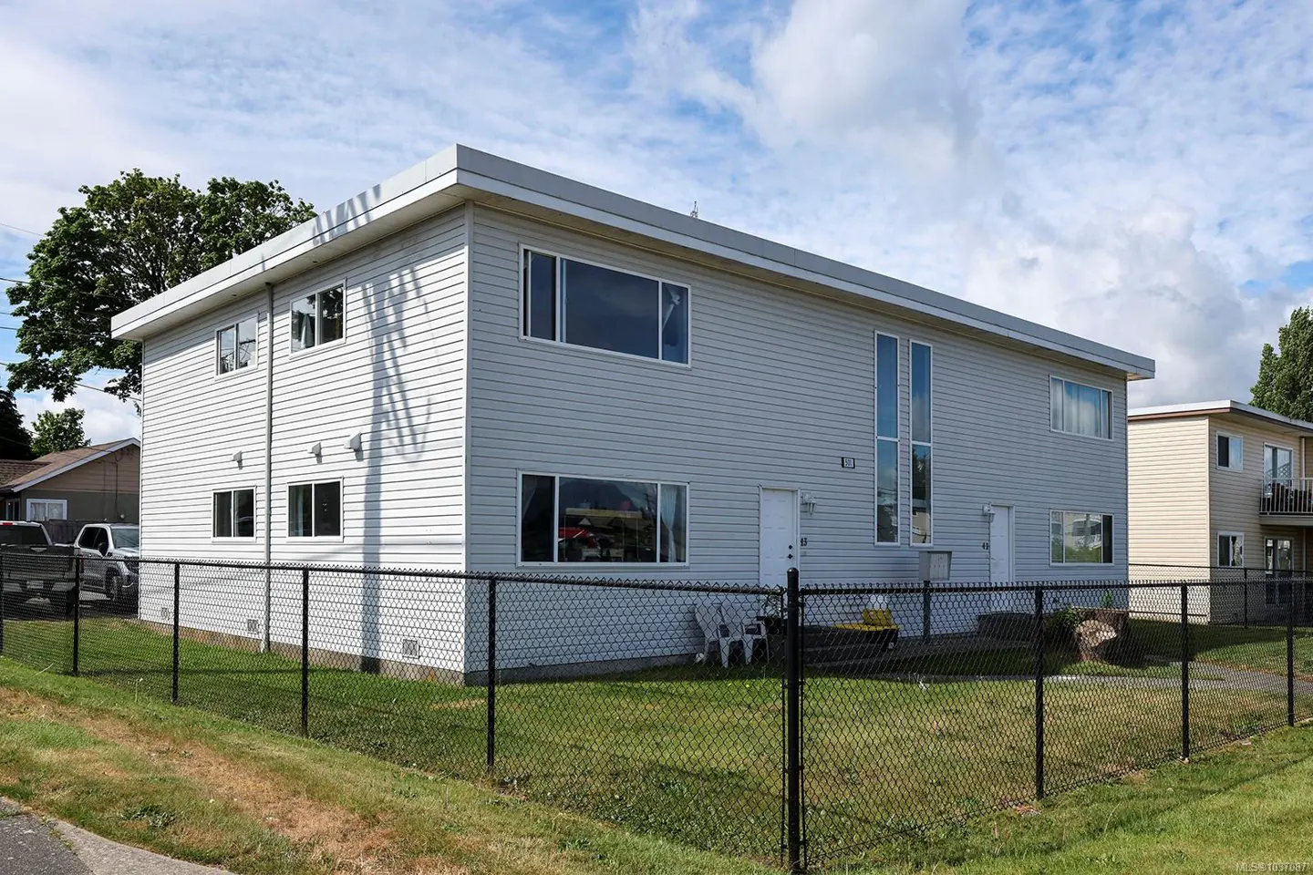 Two-story light gray apartment building with a black chain link fence and green lawn.