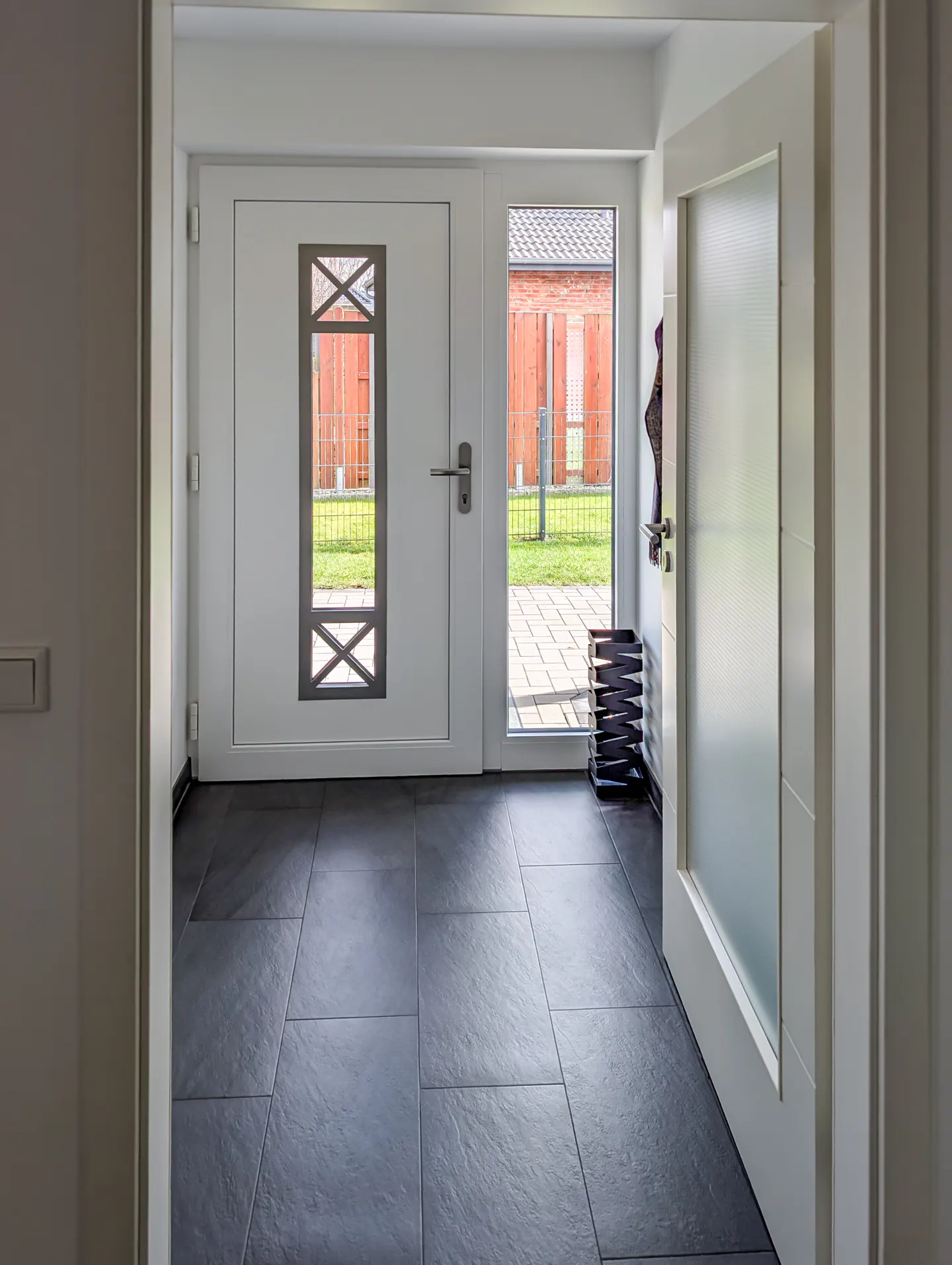 Entryway with gray tile floor, white front door with window, and open side door to the outside.