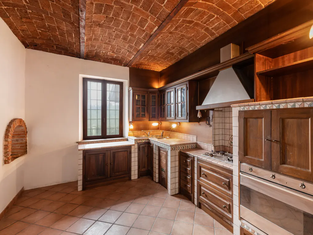 A rustic kitchen with dark wood cabinets, tiled countertops, and a brick barrel-vaulted ceiling.