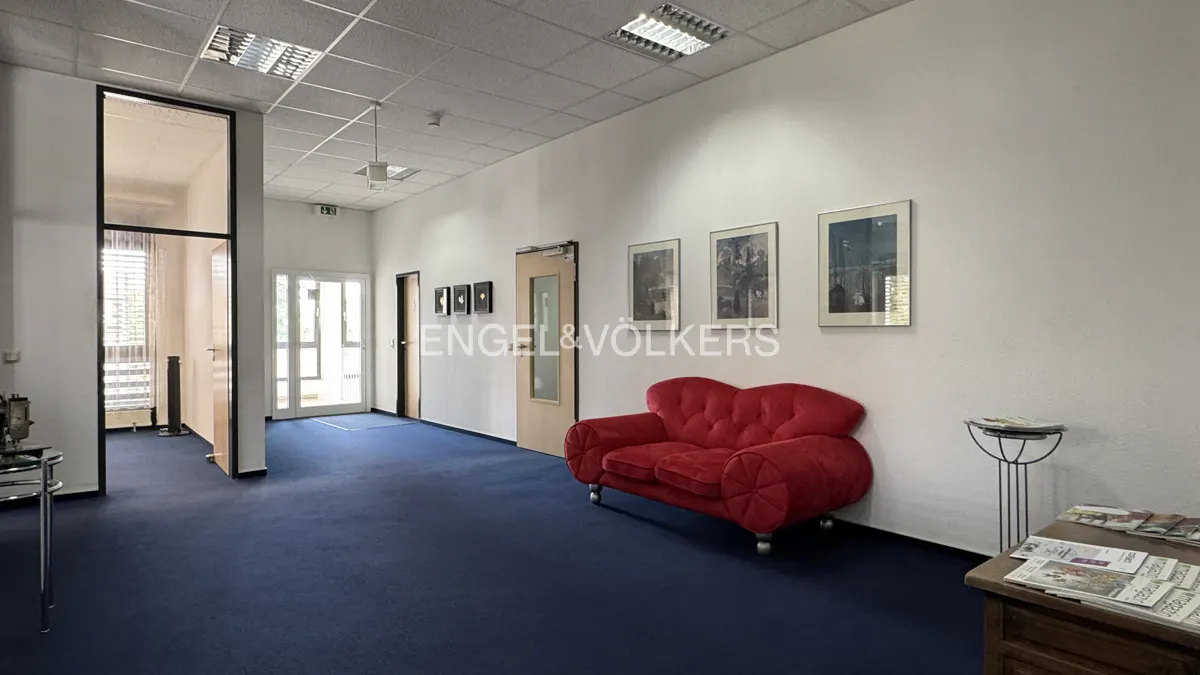 A real estate office lobby with blue carpet, white walls, and a red sofa. Artwork hangs on the wall.