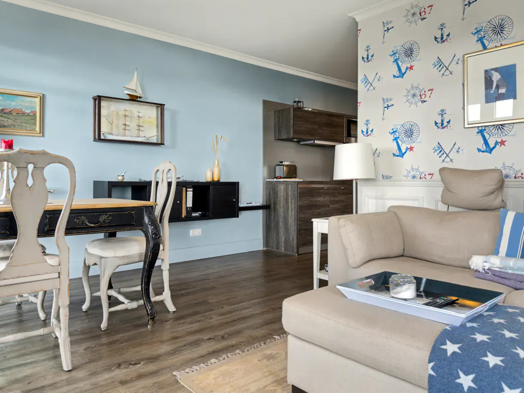 Living room with nautical theme. Blue walls, anchor wallpaper, wood floors, and a beige sofa with a blue star blanket.
