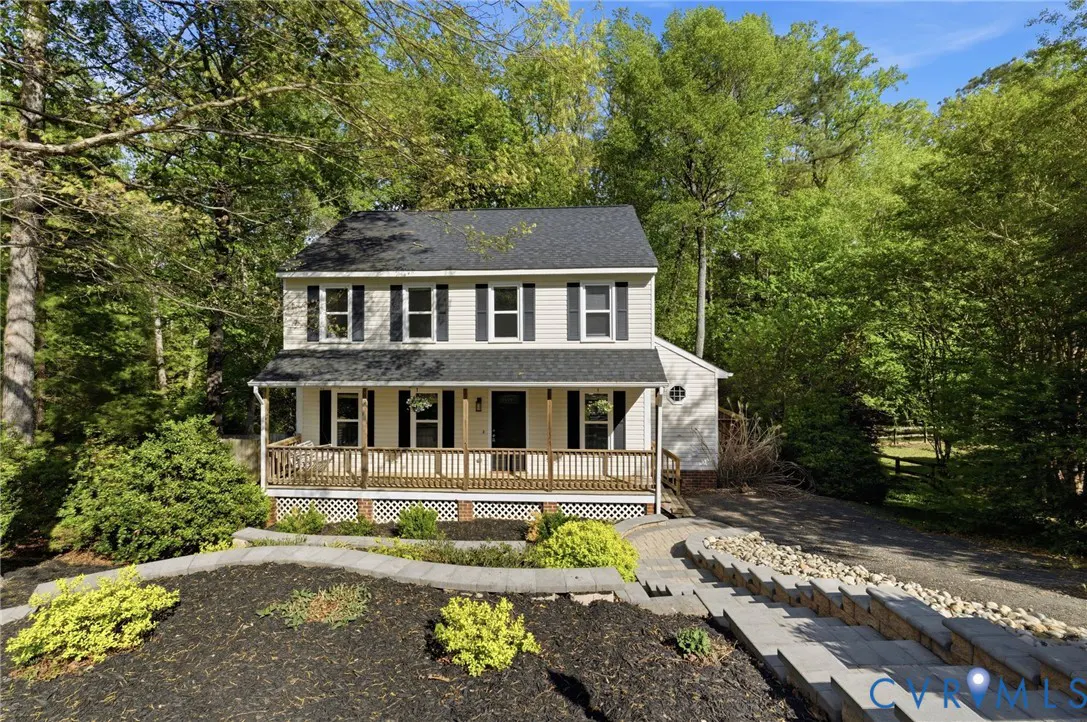 Two-story house with a black roof, white siding, and black shutters, surrounded by green trees. A wooden porch is in front.