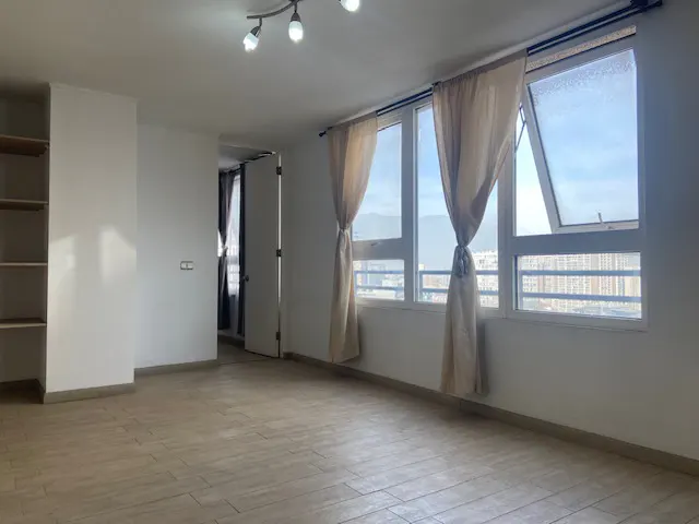 Bright, empty room with light tile floors, white walls, beige curtains, and large windows overlooking a city skyline.