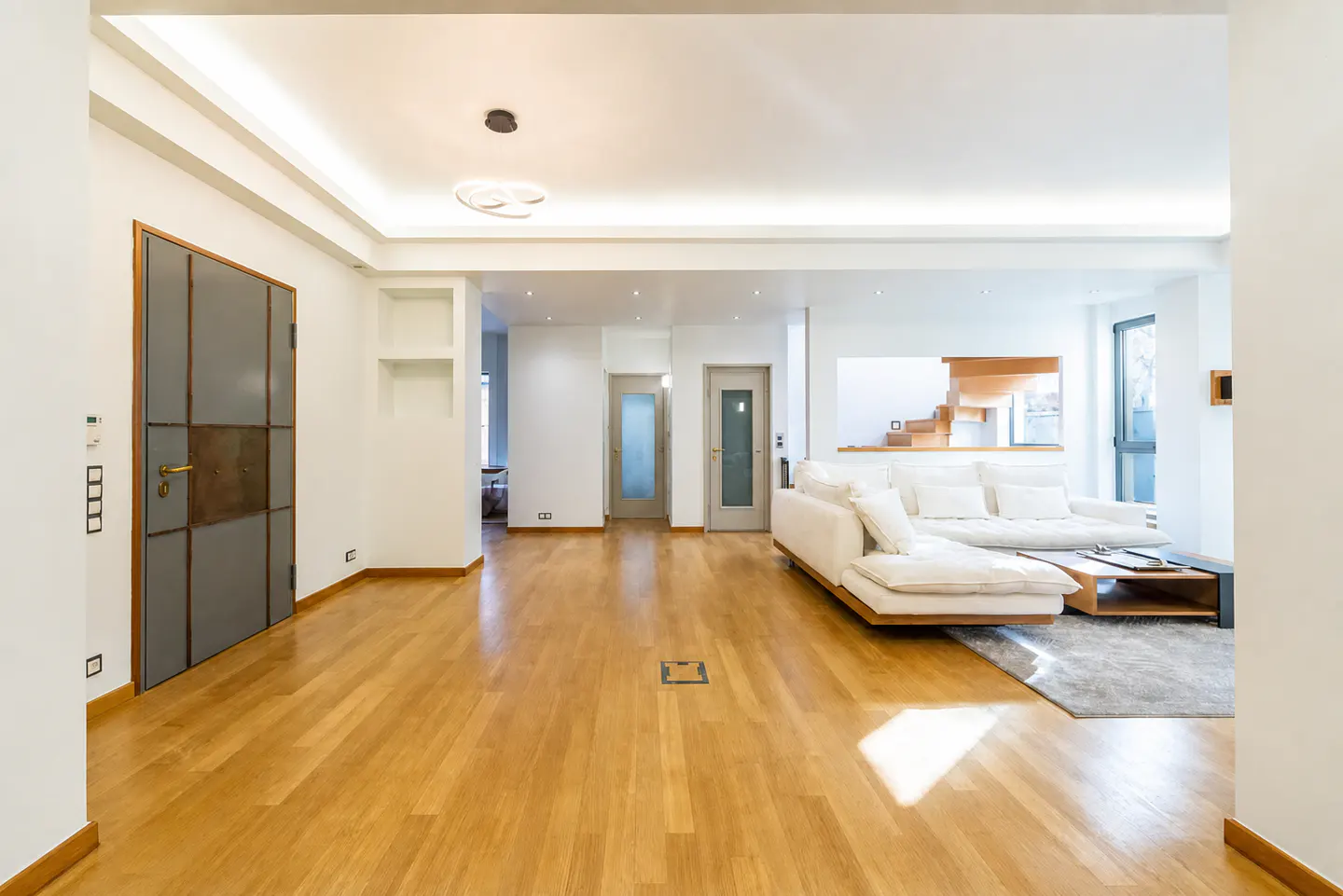 Modern living room with hardwood floors, a white sectional sofa, and a grey paneled door in a bright, open-plan space.