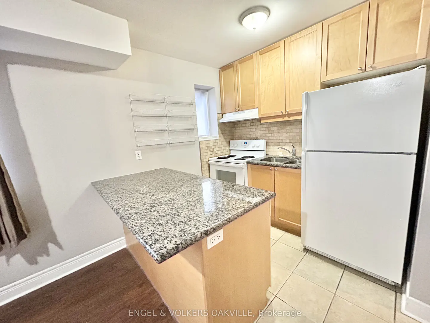 A kitchen with light wood cabinets, white appliances, and a granite-topped island.