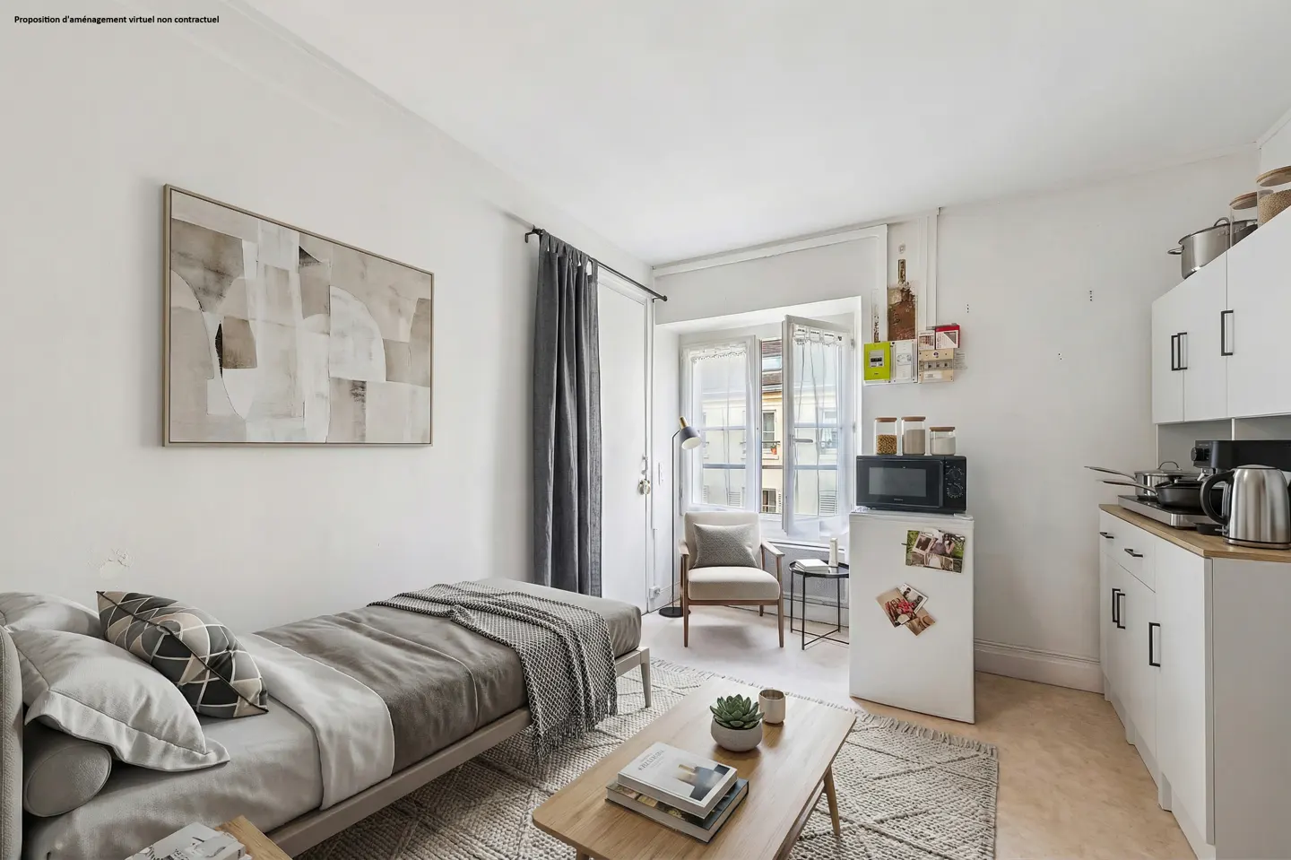 Bright studio apartment with a daybed, abstract art, and a small kitchen area with white cabinets and appliances. A window provides natural light.