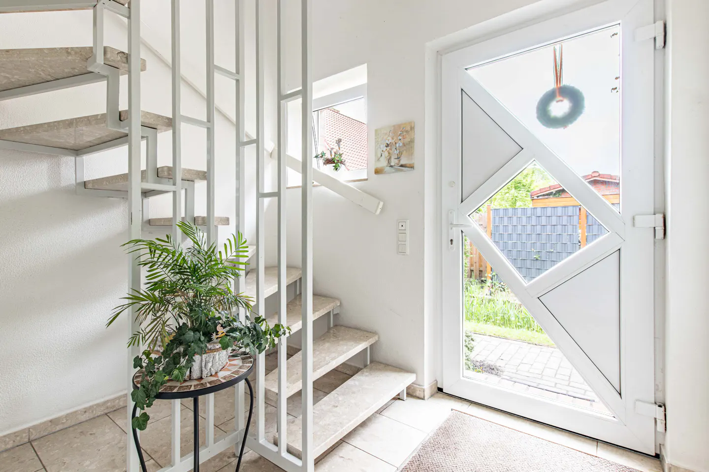 Bright foyer with white geometric door, wreath, and stairs with a plant on a mosaic table.
