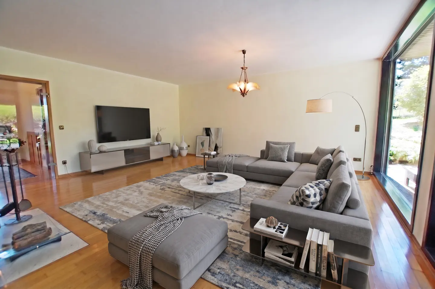 Spacious living room with a grey sectional sofa, marble coffee table, large TV, and floor-to-ceiling windows.
