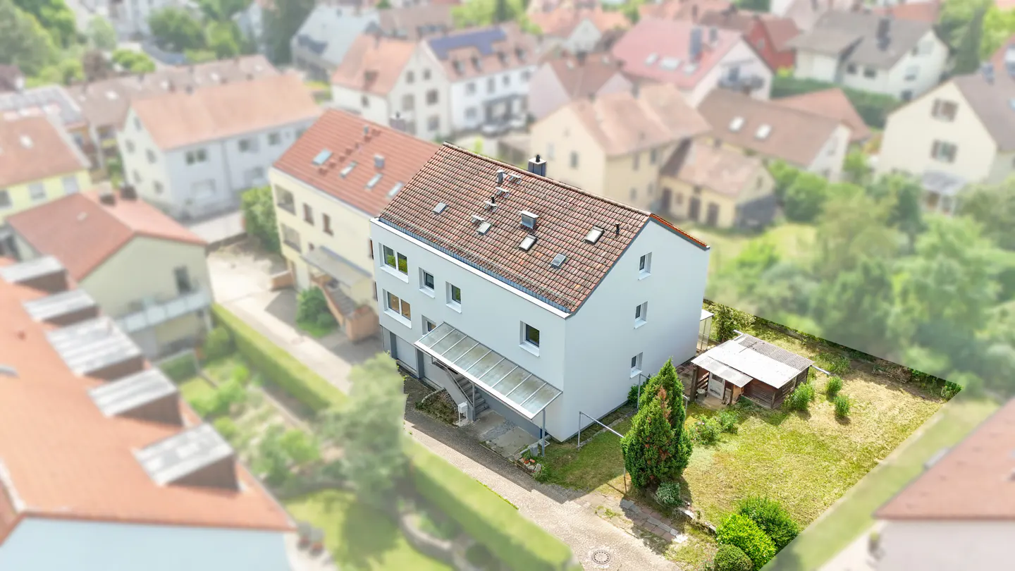 Aerial view of a light gray two-story house with a red tile roof and a small green yard.