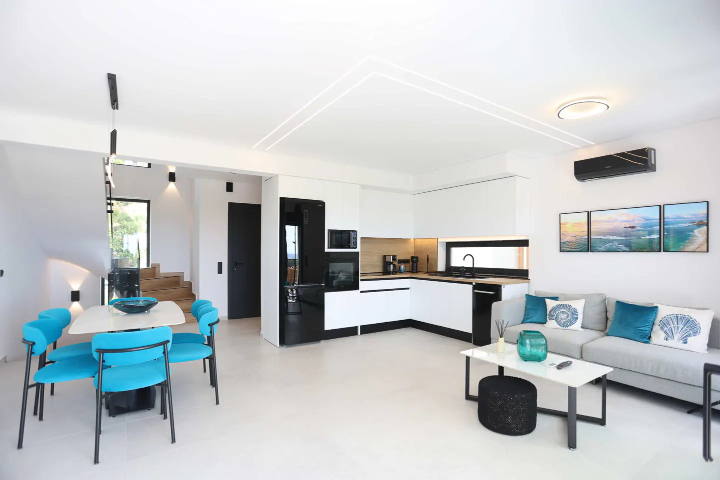 Bright, modern open-concept living space with white walls, black accents, and turquoise chairs. Kitchen, dining, and living areas are visible.