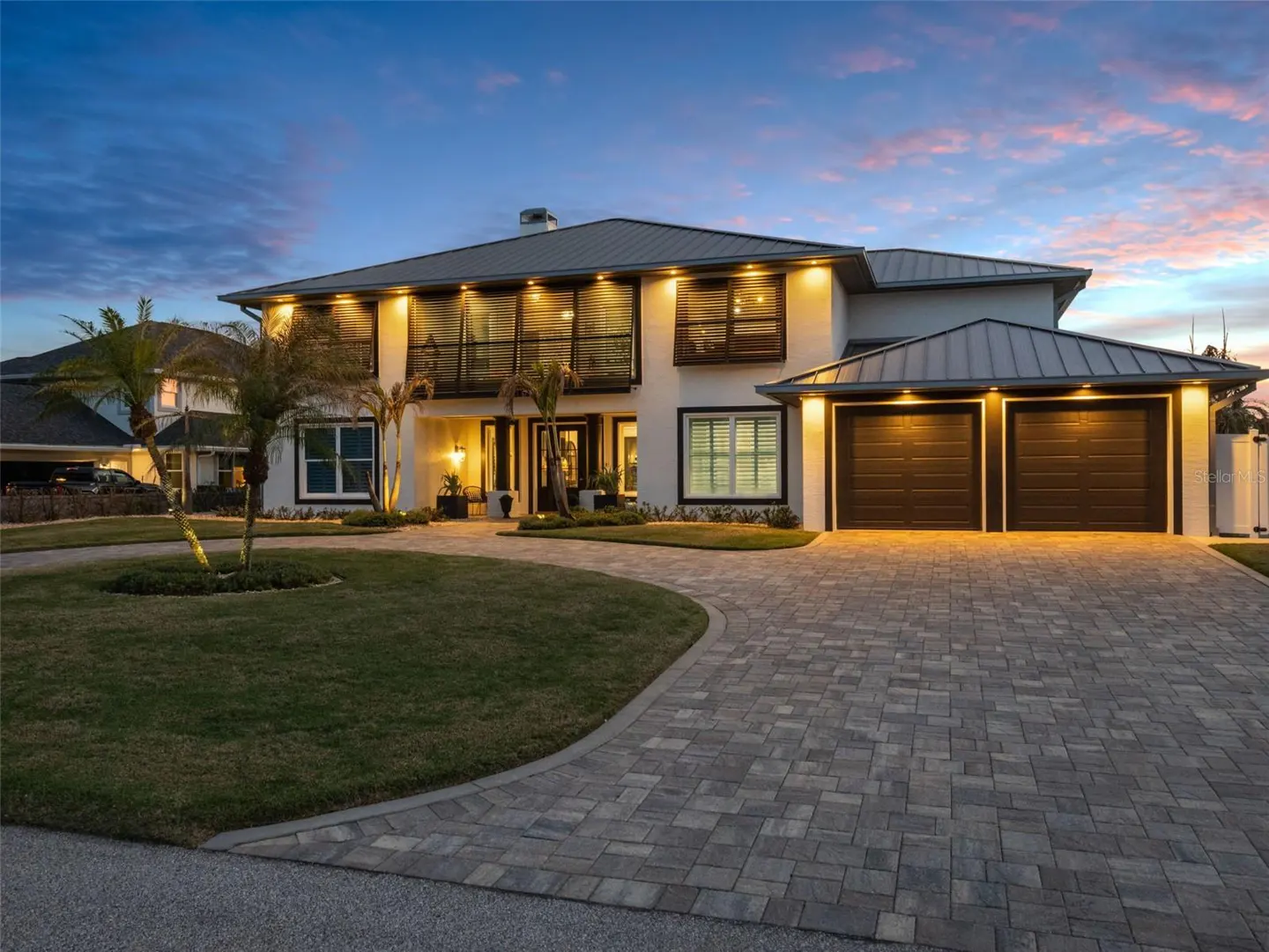 Two-story white house with a gray roof, black trim, and a brick driveway at dusk.
