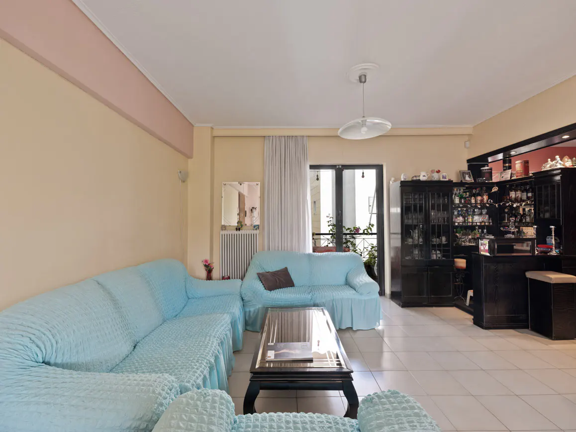 Living room with light blue sofas, a dark wood coffee table, and a black bar area with shelves of bottles.