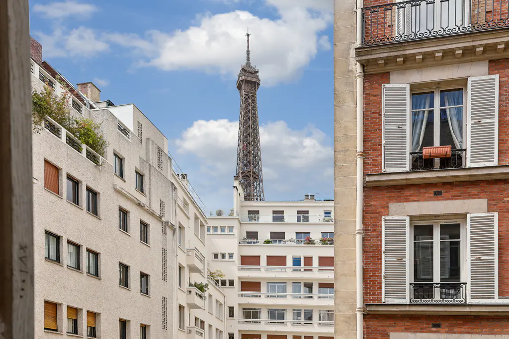 View of the Eiffel Tower framed by Parisian apartment buildings with white and red brick facades under a blue sky.