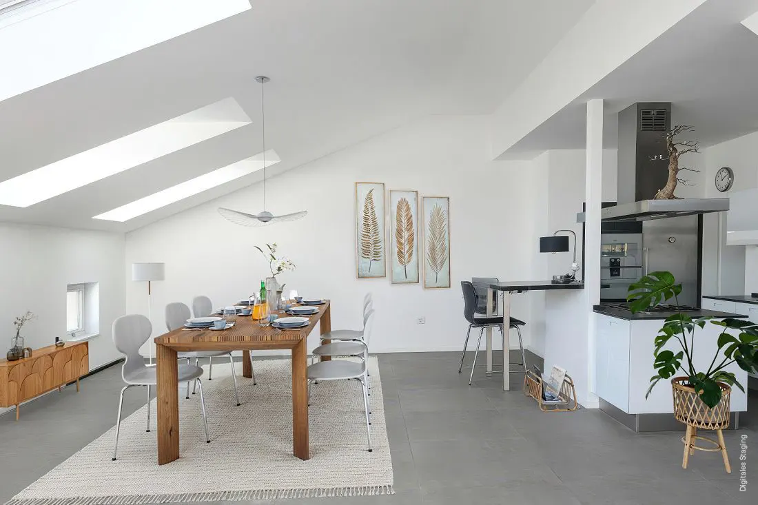 Bright, modern dining area with a wooden table set for a meal, surrounded by gray chairs on a white rug. Skylights and fern art add to the airy feel.