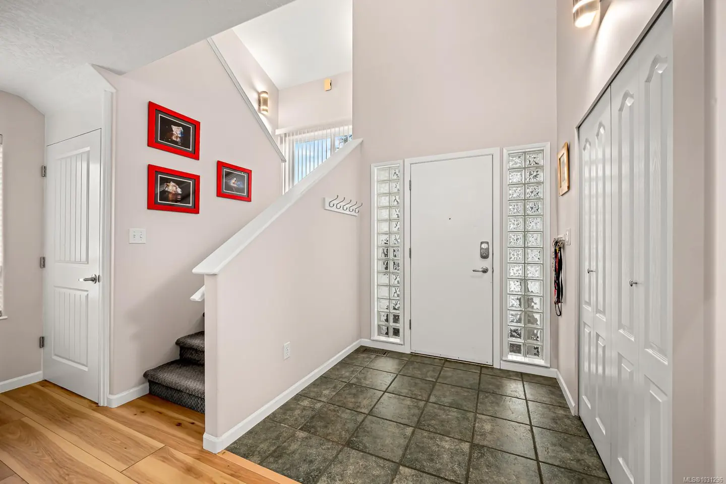 Entryway with tile floor, white door with glass blocks, and stairs with red-framed pictures.