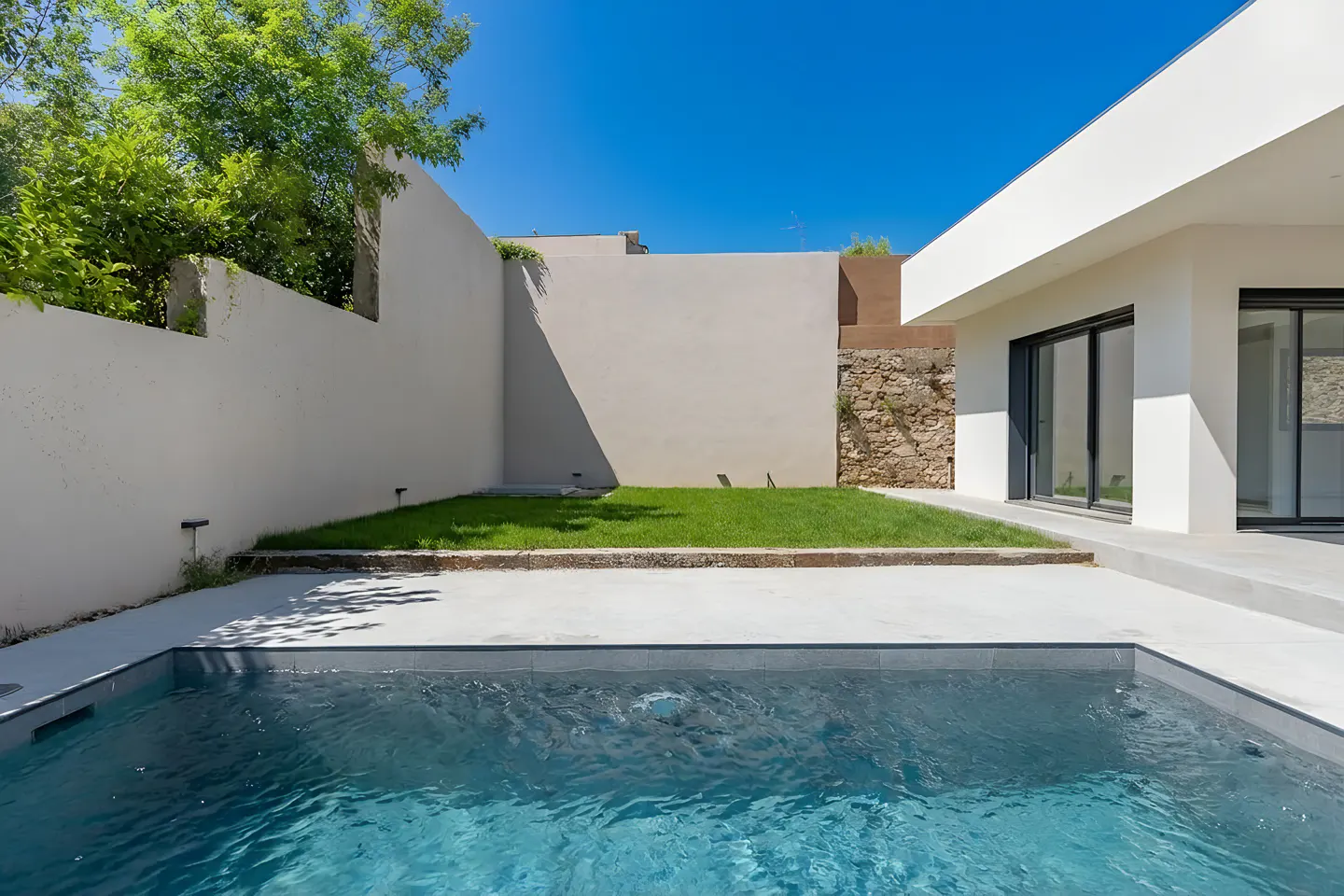 Modern home exterior with a blue swimming pool, white walls, green grass, and a clear blue sky.