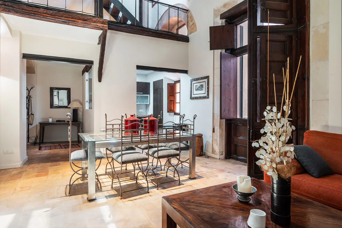 Bright living area with a glass dining table, orange sofa, terracotta floors, and dark wood accents in a historic home.