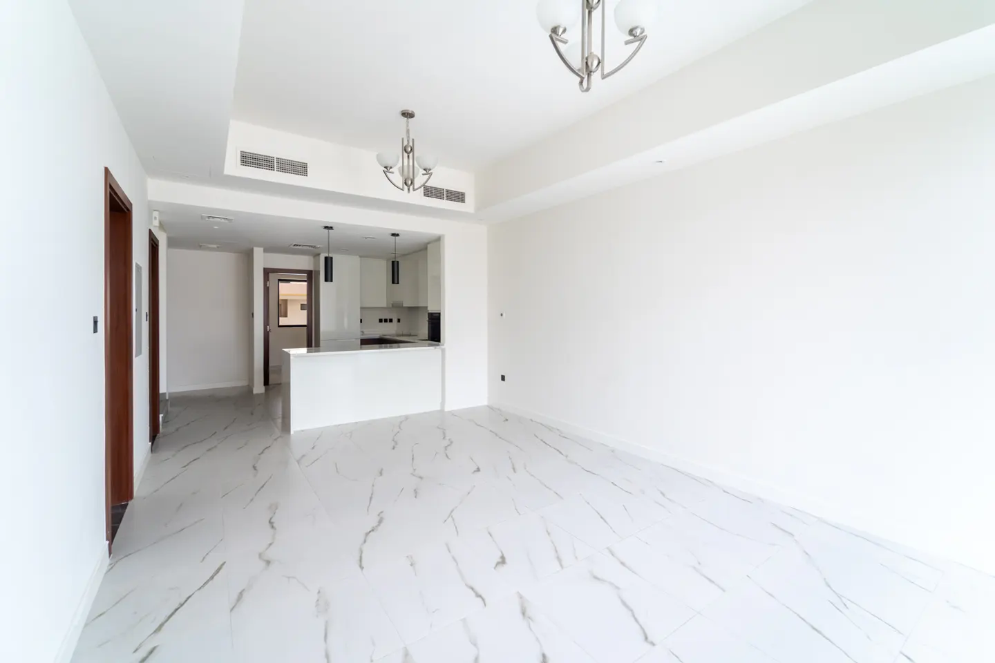 Bright, empty apartment with white walls, marble floors, and a kitchen with a breakfast bar in the background.