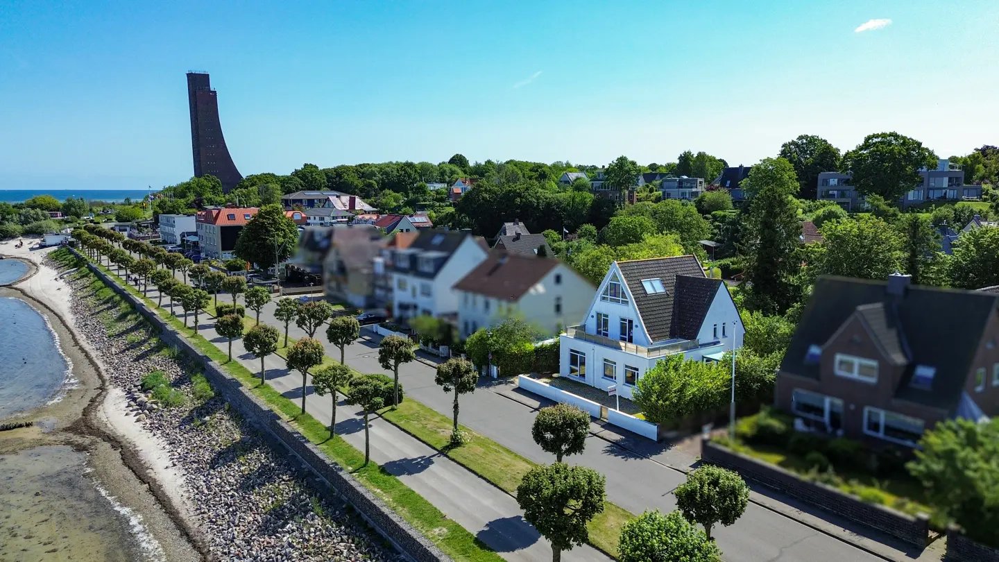 Aerial view of a white house with a gray roof near the ocean and a tall monument.