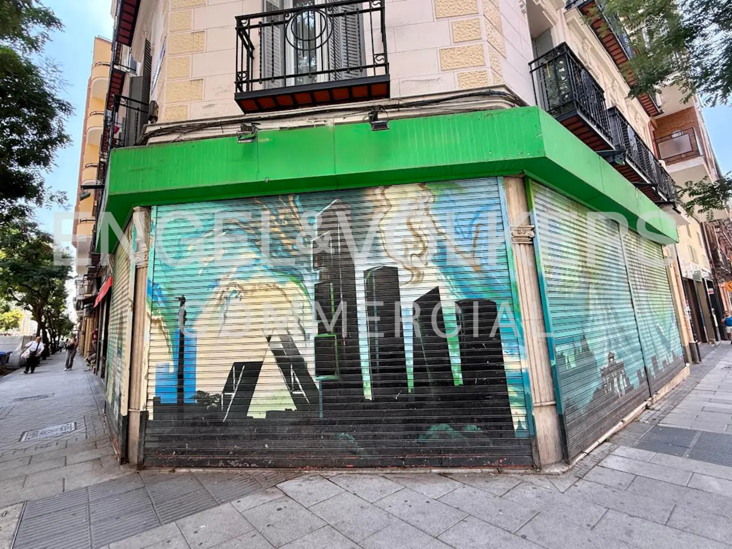 Closed storefront with green trim and painted metal shutters featuring a city skyline mural.