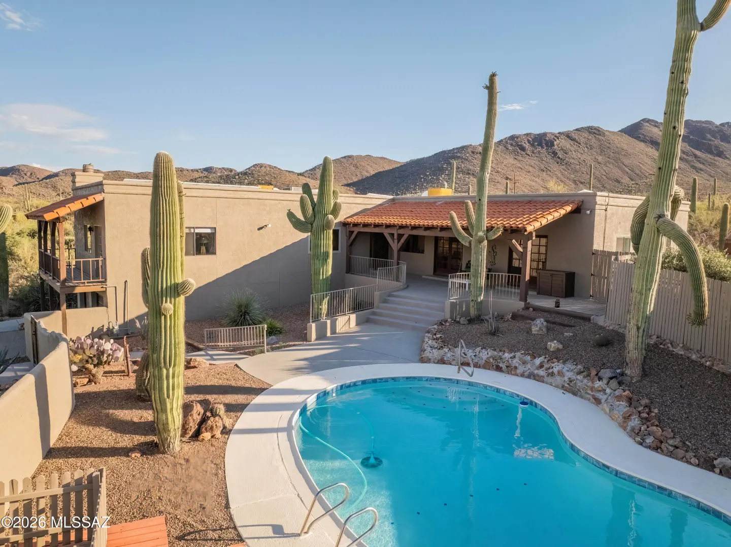 Exterior view of a desert home with a pool, cacti, and mountain backdrop under a clear blue sky.