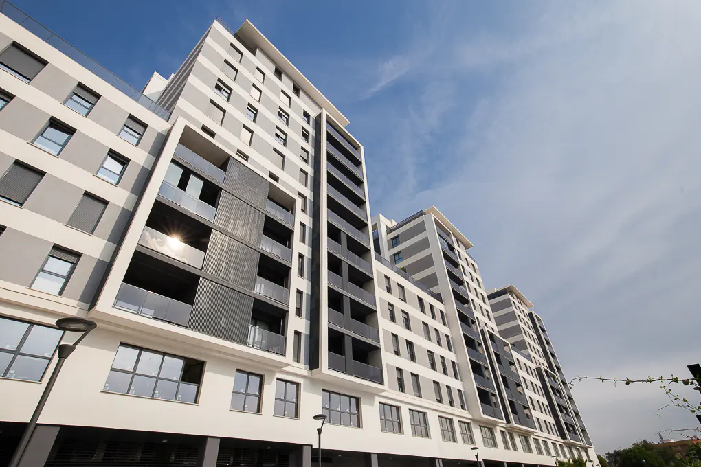 Modern apartment building with gray and white horizontal stripes under a blue sky. Balconies have dark gray railings.