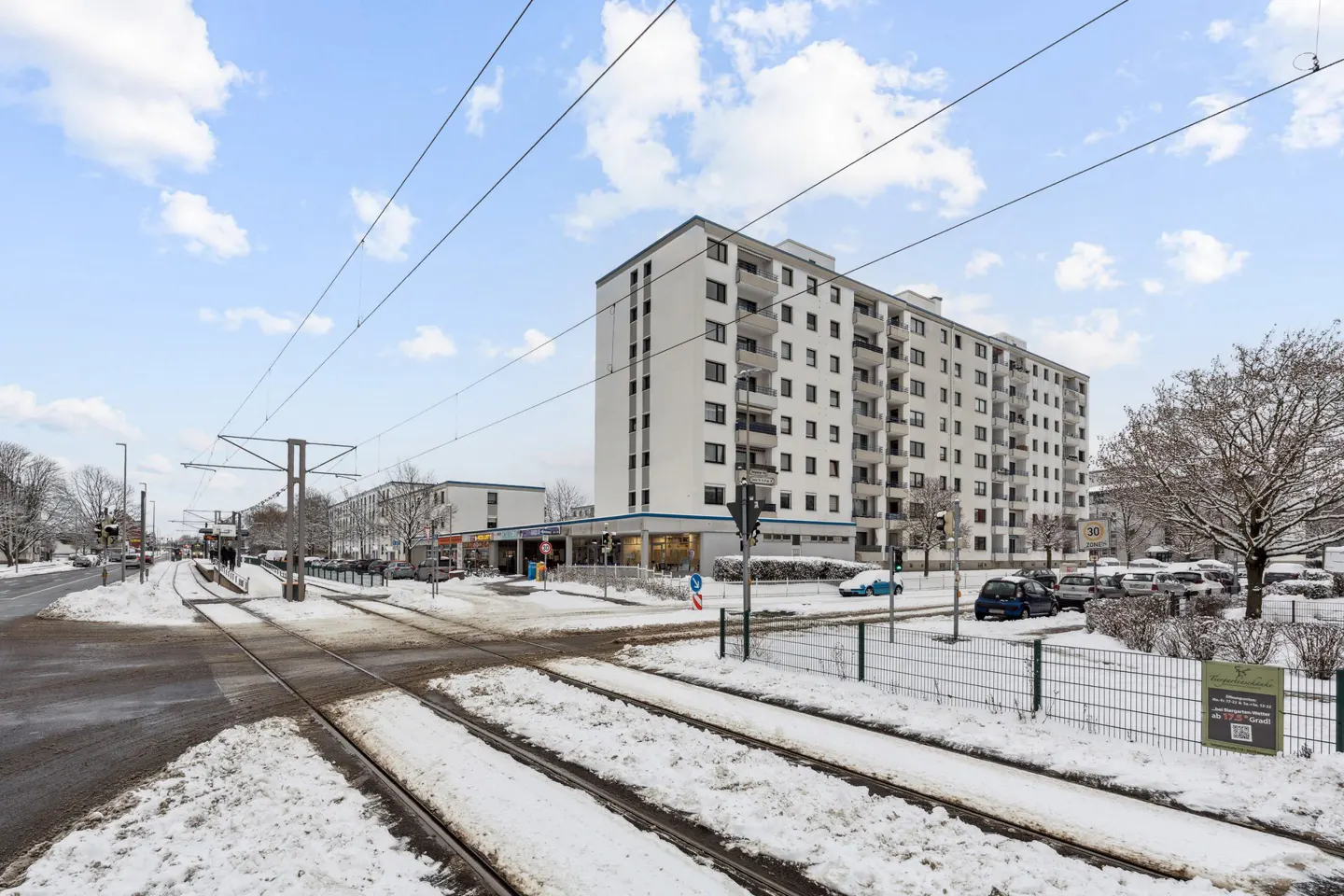 Exterior view of a white apartment building with tram tracks covered in snow in the foreground.
