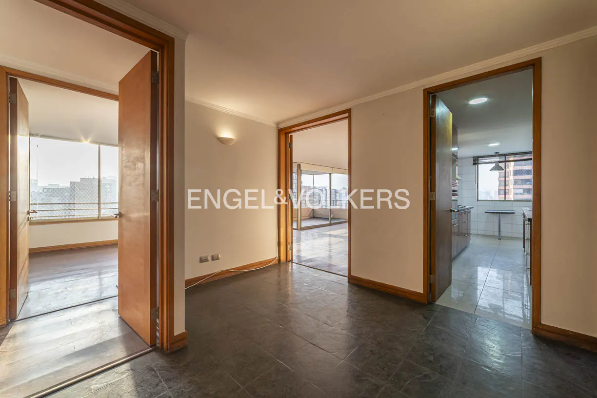 A bright, empty room with dark floors and three open doorways. The Engel & Volkers logo is superimposed on the image.