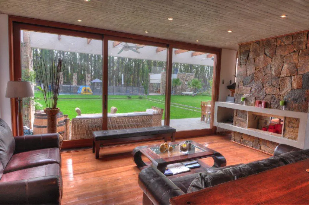 Living room with wood floors, stone fireplace, and large glass doors to a green lawn with trees.