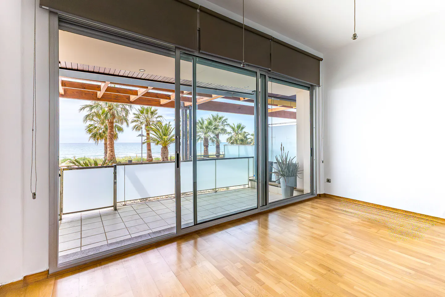 Bright room with hardwood floors and large sliding glass doors opening to a balcony with ocean views and palm trees.