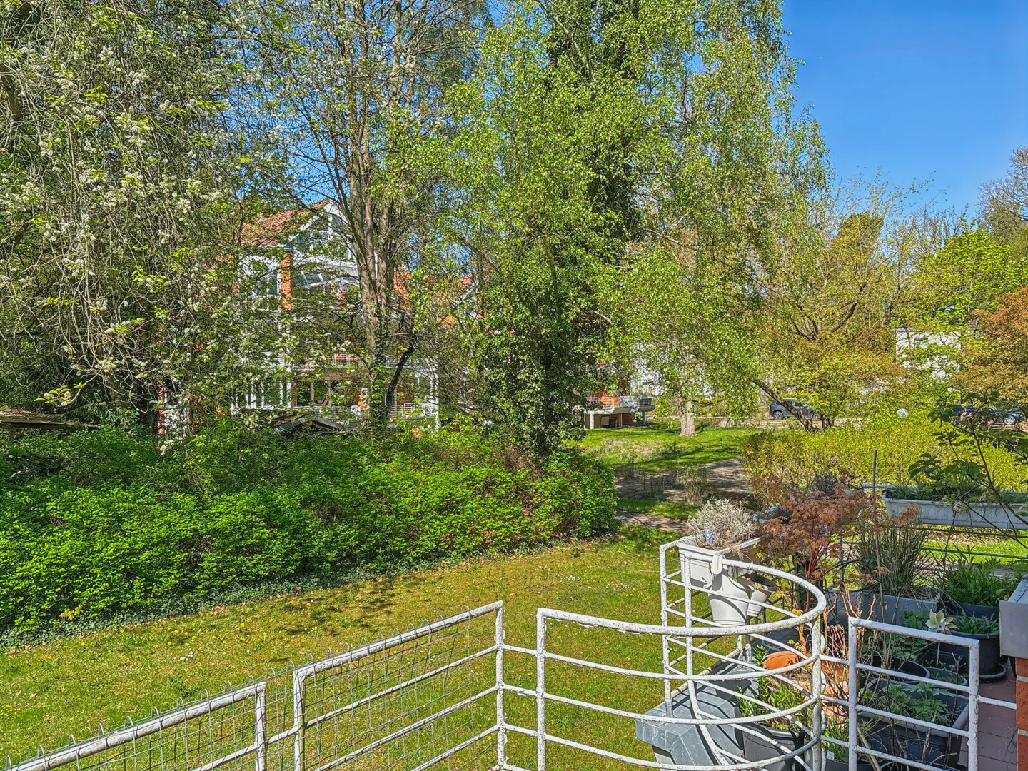 View from a white balcony overlooking a green lawn, trees, and a house in the background.