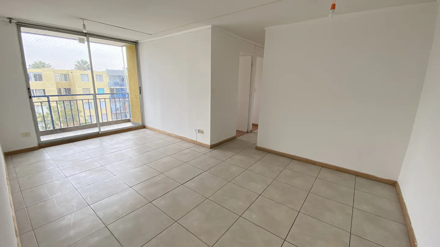 Empty room with white walls, light-colored tiled floors, and a sliding glass door leading to a balcony with a city view.
