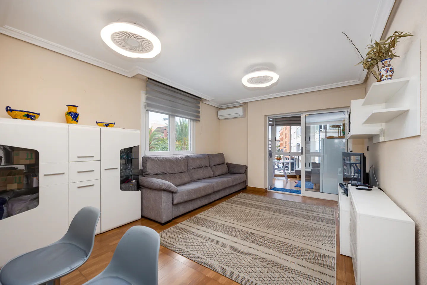 Living room with gray sofa, striped rug, white cabinets, and two gray chairs. Balcony visible through sliding glass door.