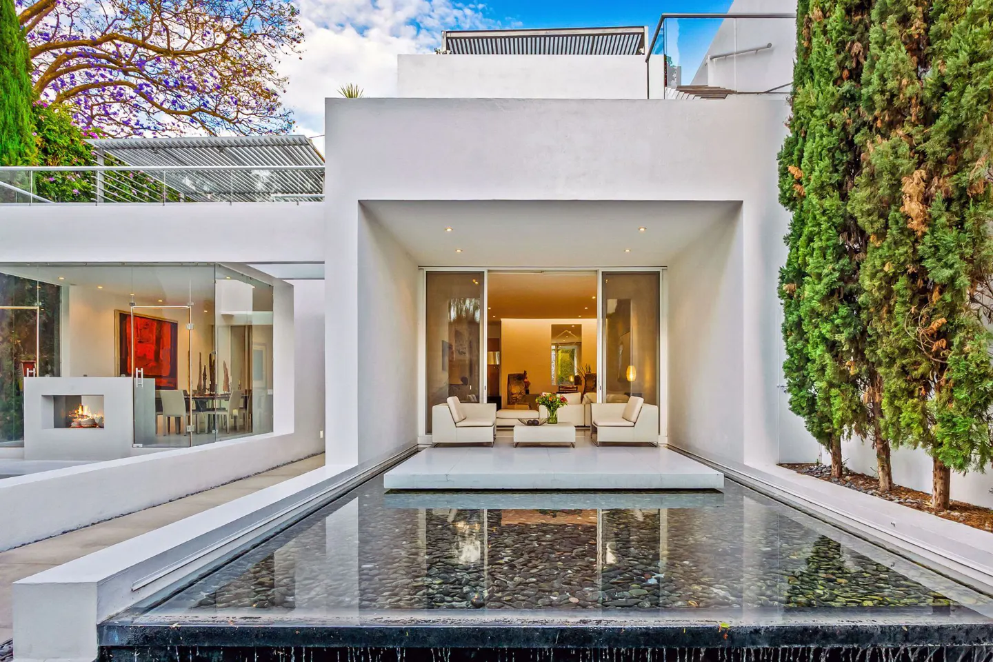 Modern white house exterior with a reflecting pool, patio furniture, and sliding glass doors.